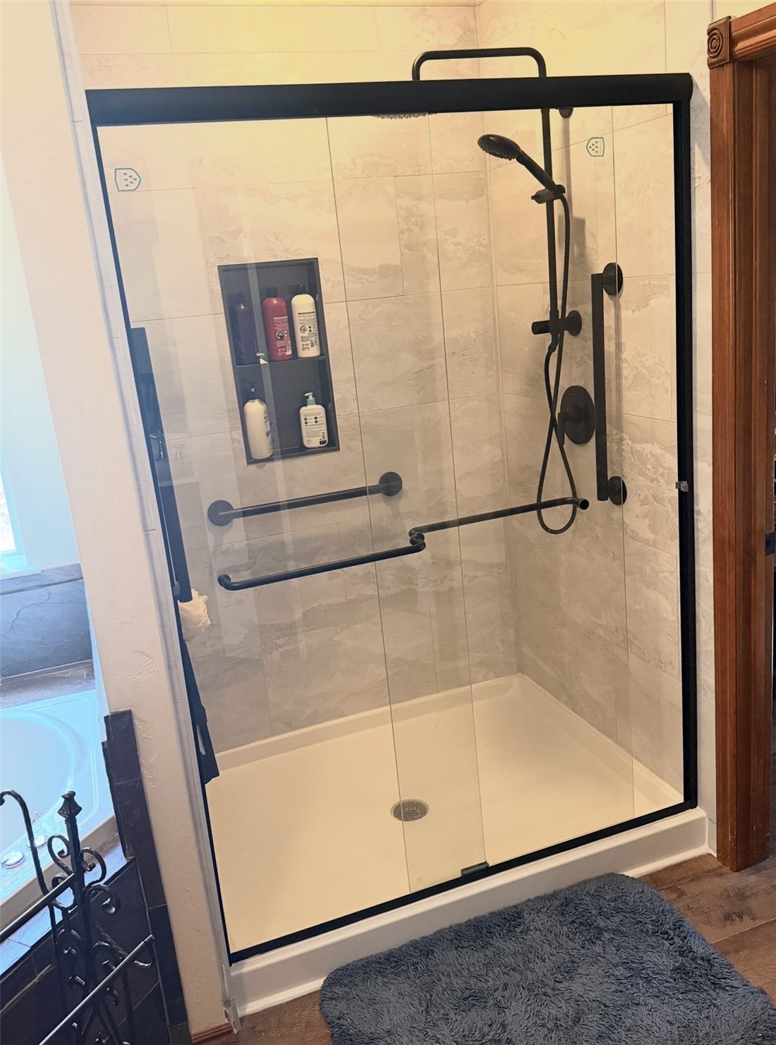 Key Signature tub-to-shower conversion in Oklahoma City: white marble-look large-format tile, black sliding glass door, recessed niche and matte black fixtures