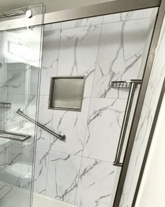 Completed shower with marble-look panels, recessed niche, and a brushed nickel sliding glass door